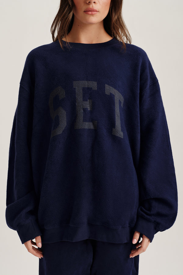 Person wearing a navy blue sweatshirt with 'SET' printed on it against a neutral background
