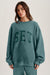 Woman wearing a teal sweatshirt with 'SET' text on a plain background <model-info>Bella wears a size XS/S and is 5’7, 23” waist, 32AB bust.</model-info> 