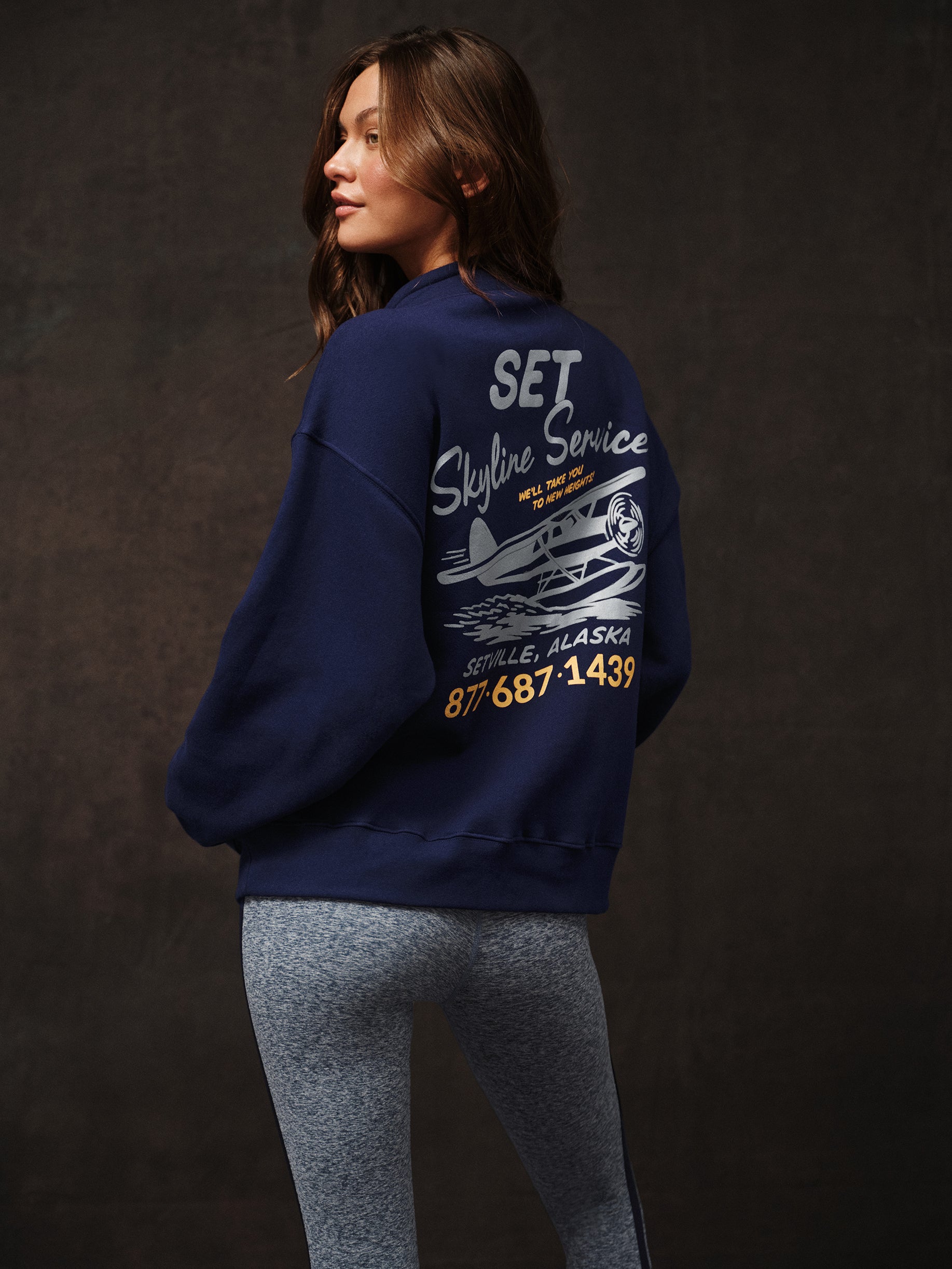 Person wearing a navy blue sweatshirt with graphics and text on the back against a dark background
