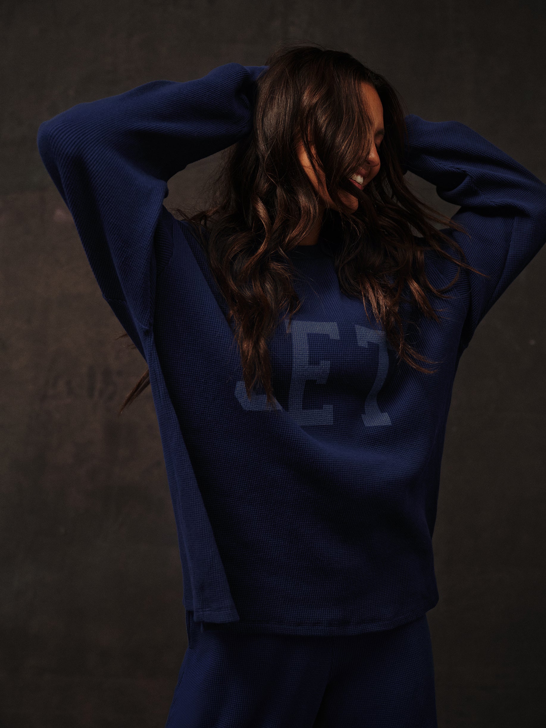 Person wearing a navy blue long sleeve with a logo on a dark background