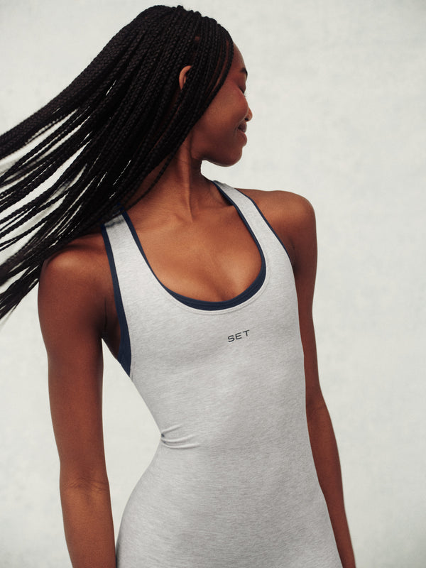 Woman wearing a gray jumpsuit with a brand logo on a plain background