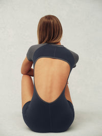 Person wearing a black one piece with a unique cutout design on a light gray background