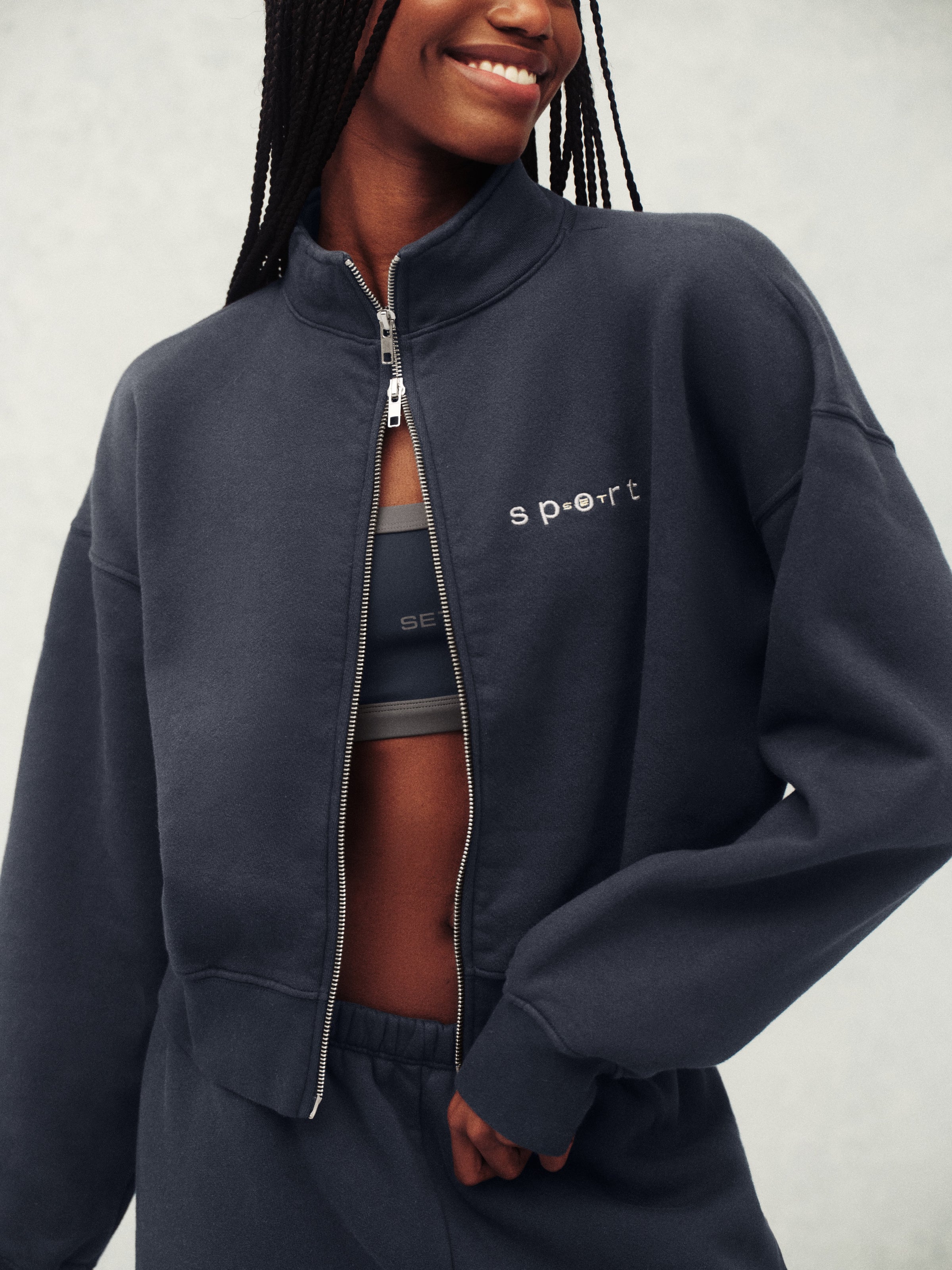 Person wearing a navy tracksuit with 'Sport' branding on a light gray background