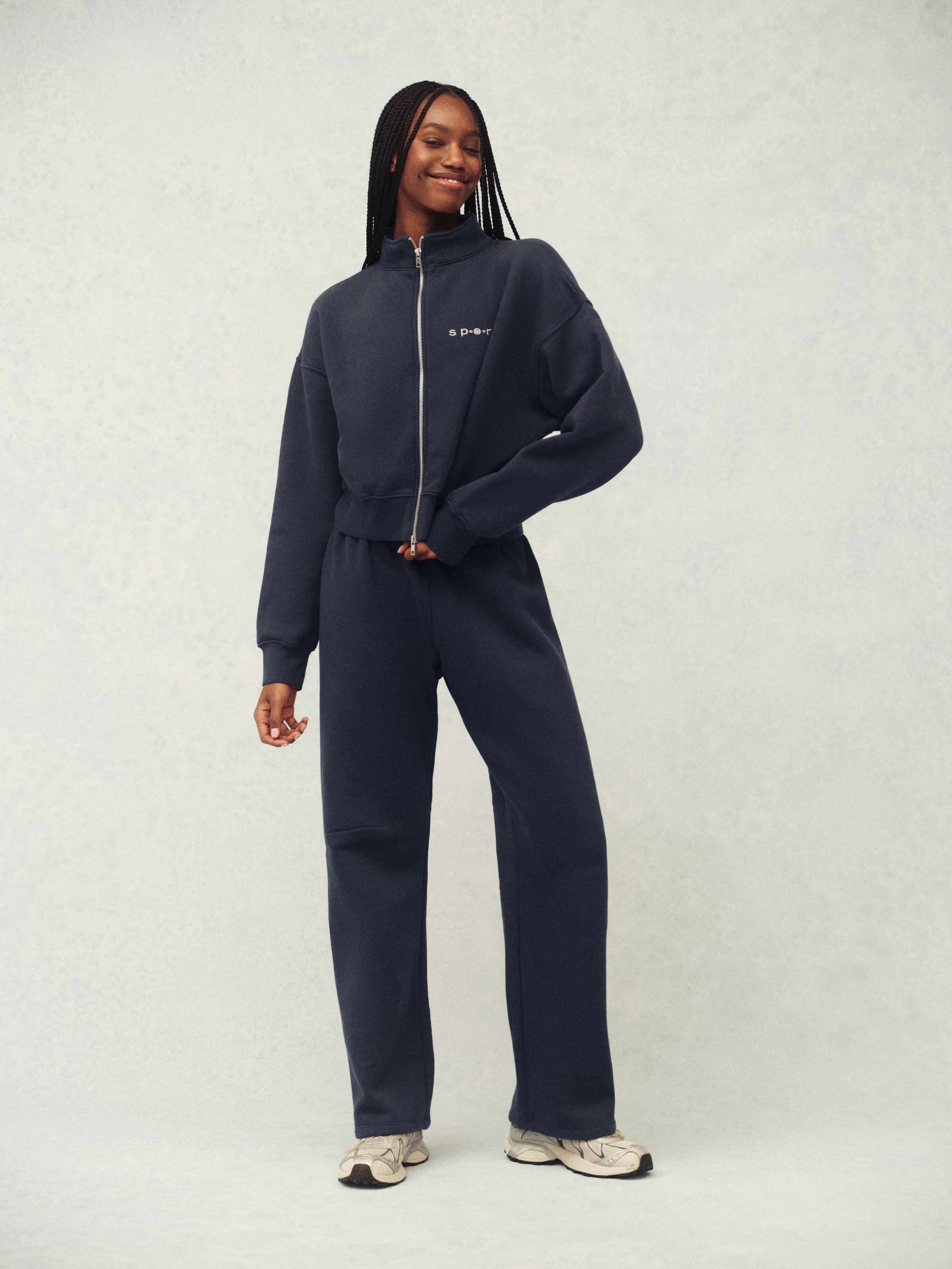 Person wearing a navy tracksuit with a white logo on a light gray background