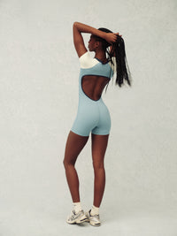 Person wearing a light blue and cream jumpsuit on a plain background