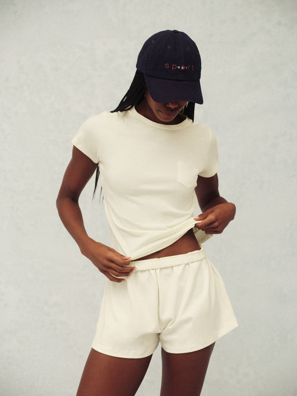 Person wearing a white t-shirt and shorts with a navy cap on a light gray background