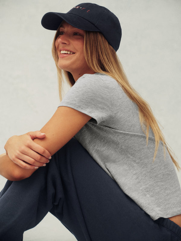 Woman wearing a navy cap and gray t-shirt sitting against a plain background