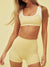 Woman wearing a yellow sports bra and shorts set on a beige background
