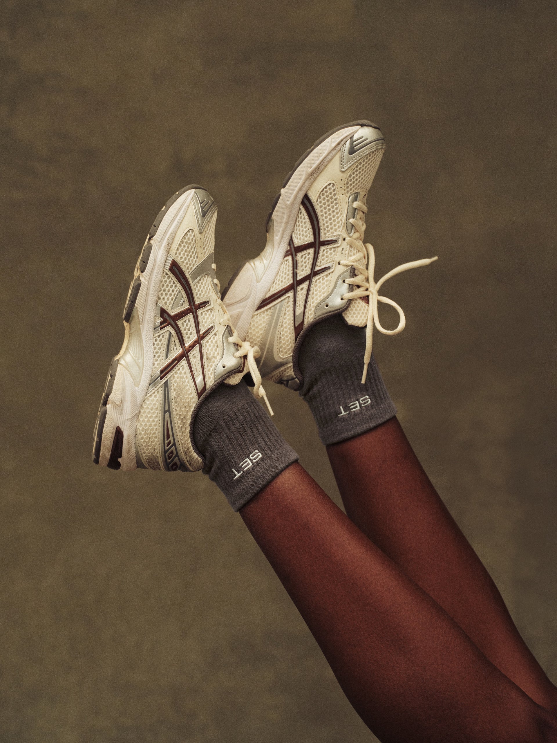 White sneakers with brown accents worn by a person against a brown background