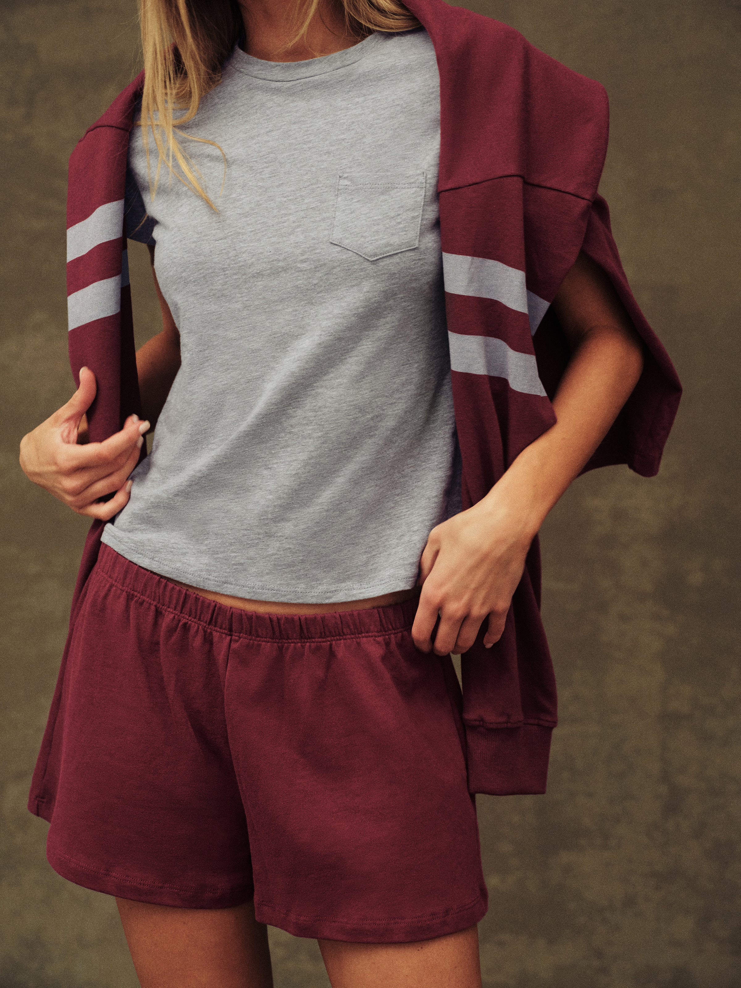 Person wearing a gray t-shirt and maroon shorts with a matching jacket over shoulders on a brown background