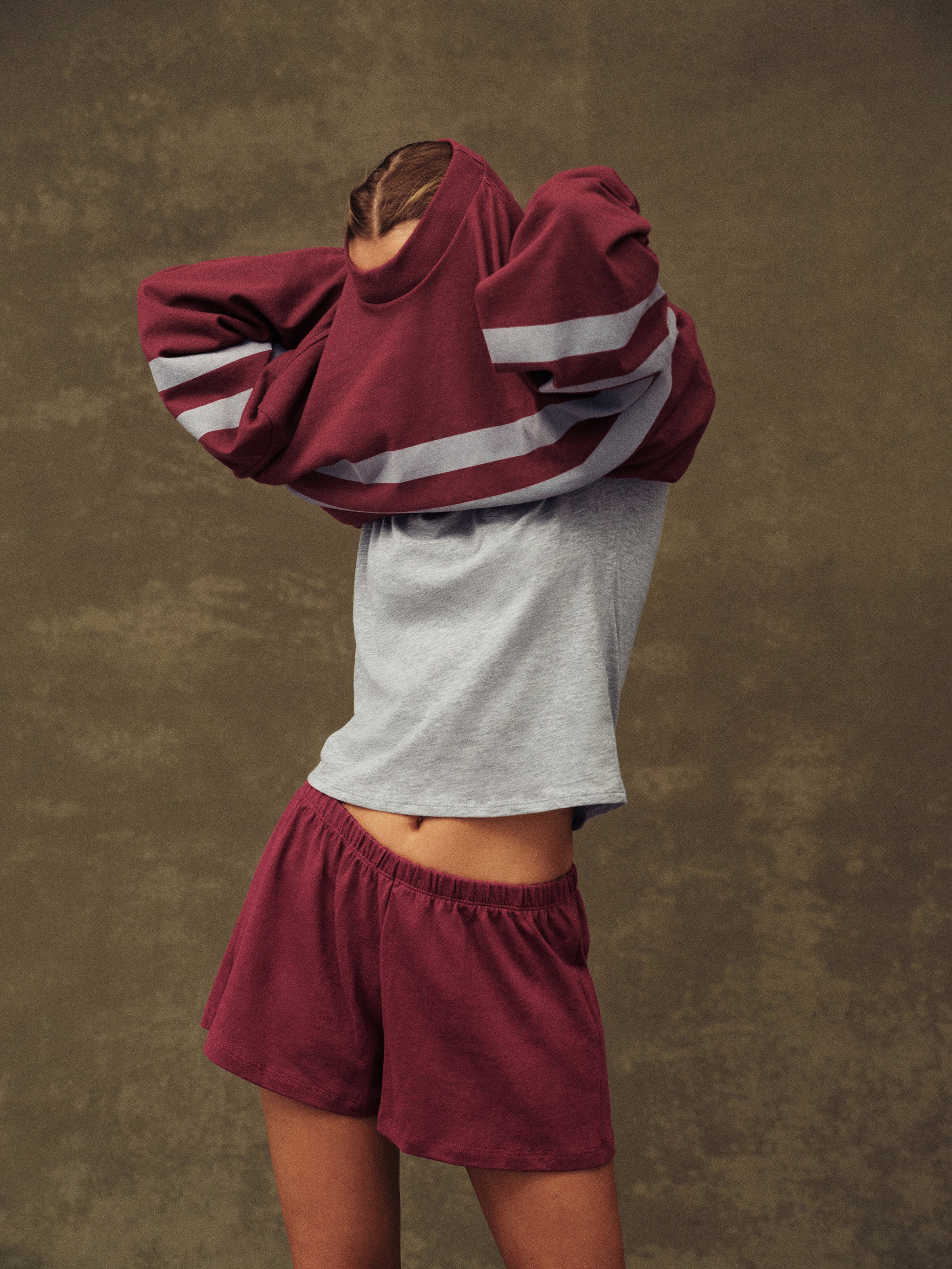 Person wearing a maroon and gray hoodie with matching shorts against a brown background