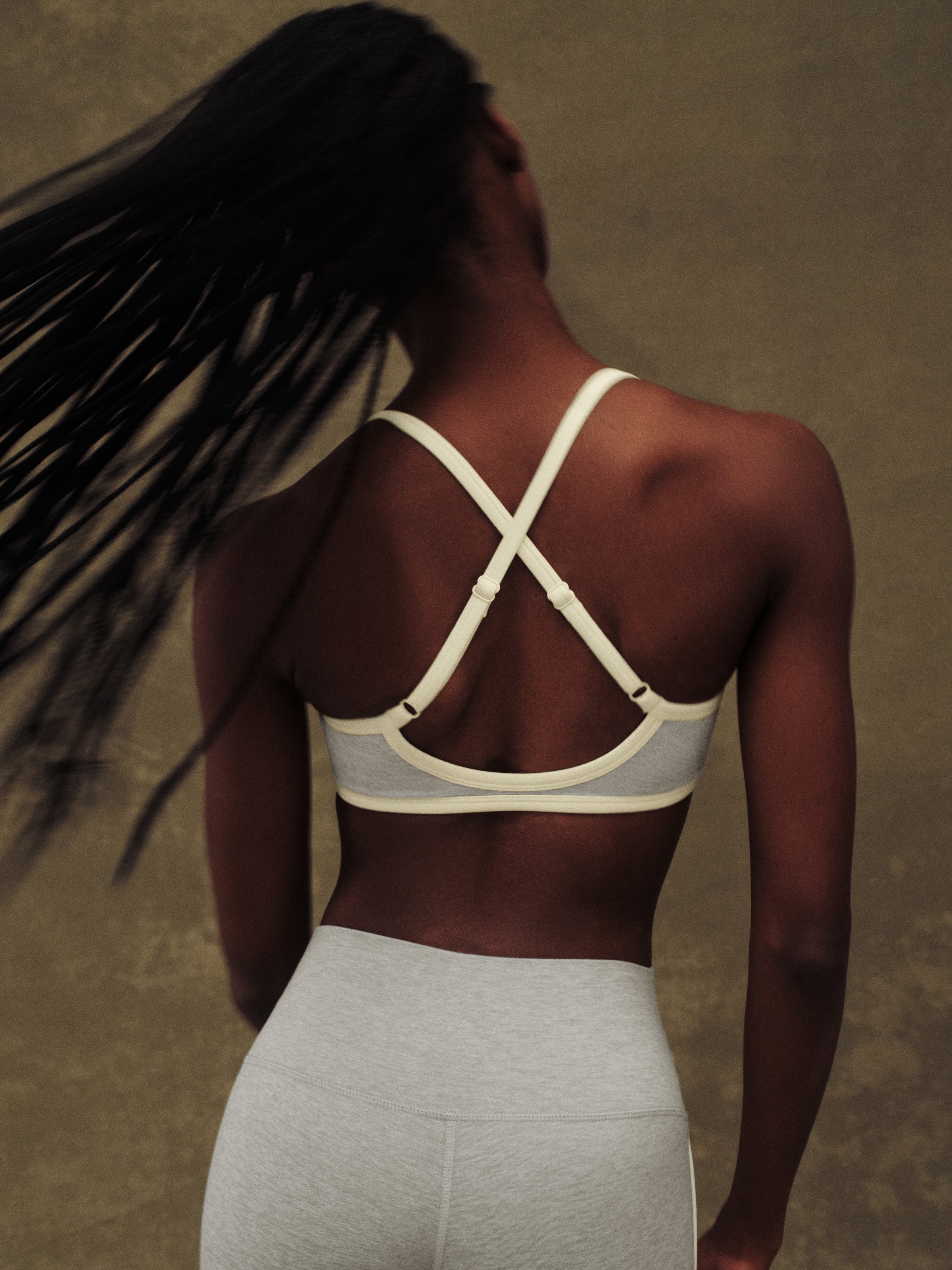 Person wearing a strappy top and white pants against a neutral background