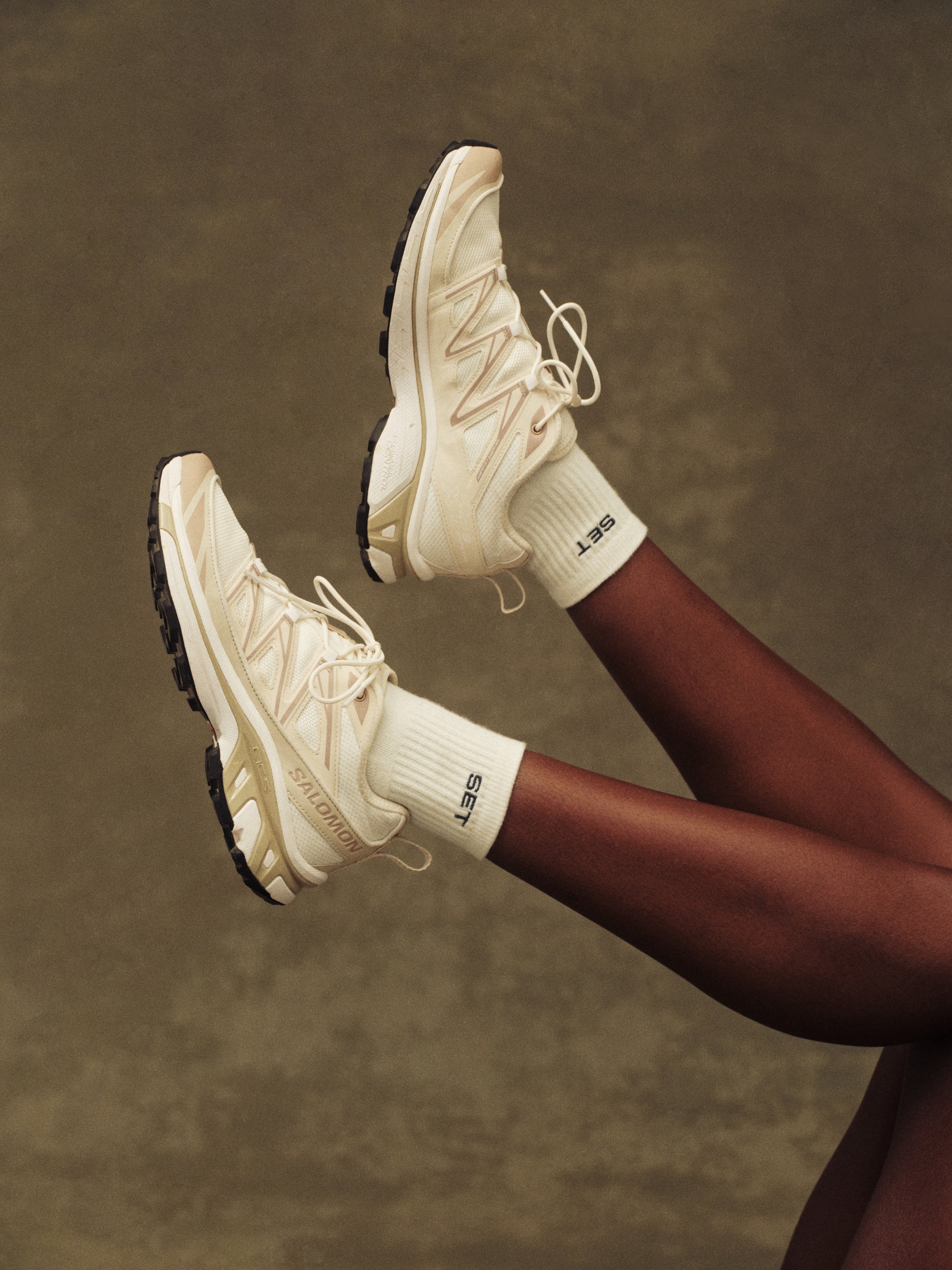 White sneakers and socks being worn against a brown background