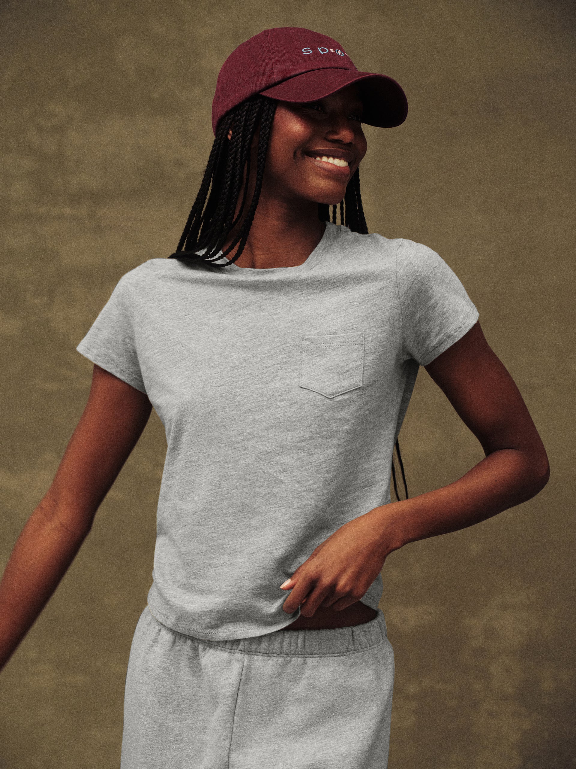 Woman wearing a gray t-shirt and maroon cap against a brown background