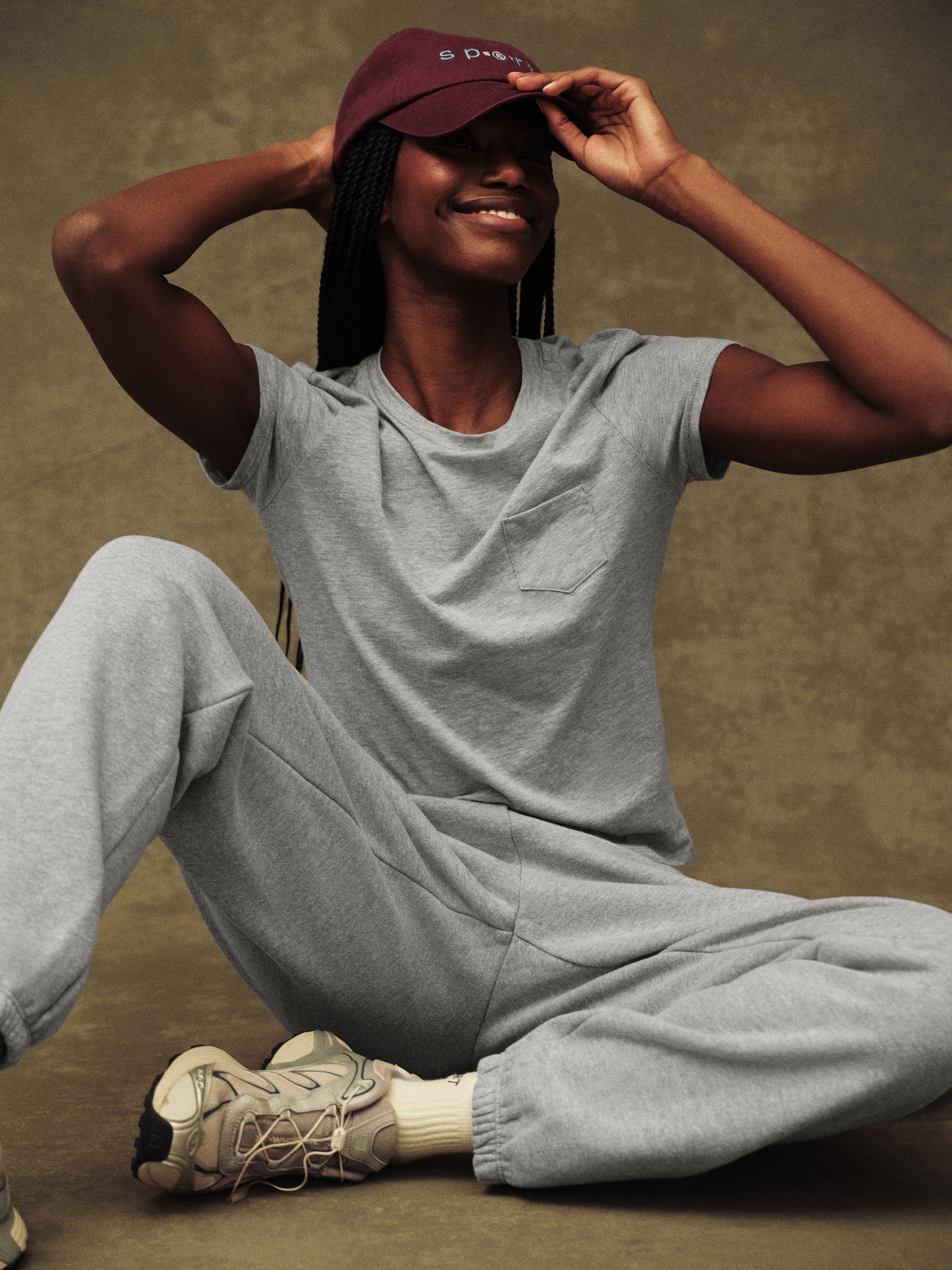 Person wearing a gray t-shirt and pants with a maroon cap on a brown background