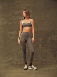 Woman wearing a gray sports bra and leggings set on a textured brown background