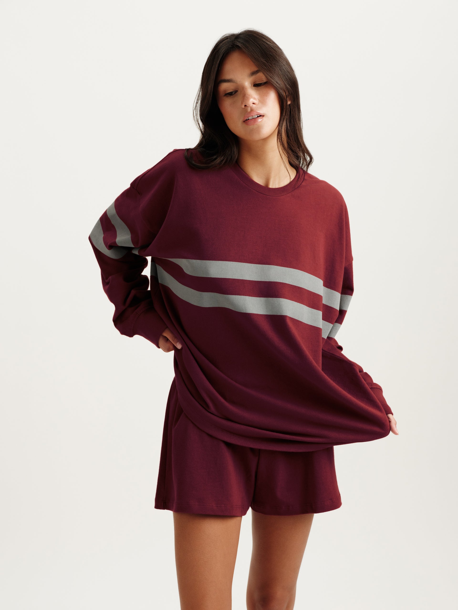 Woman wearing a maroon sweatshirt with a large white stripe and matching shorts on a light gray background <model-info>Jelene wears a size S and is 5’7”, 23” waist, 32AB bust.</model-info>