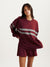 Woman wearing a maroon sweatshirt with a large white stripe and matching shorts on a light gray background <model-info>Jelene wears a size S and is 5’7”, 23” waist, 32AB bust.</model-info>