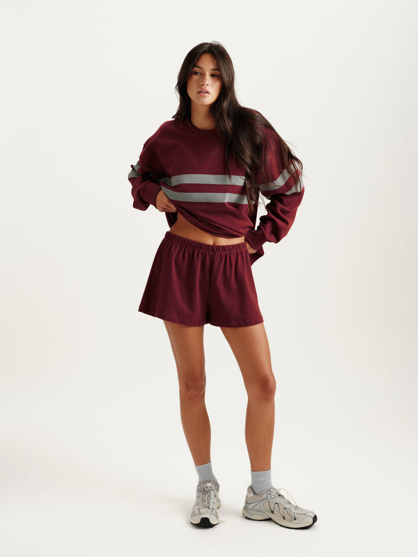 Woman wearing a maroon tracksuit with reflective stripes on a white background