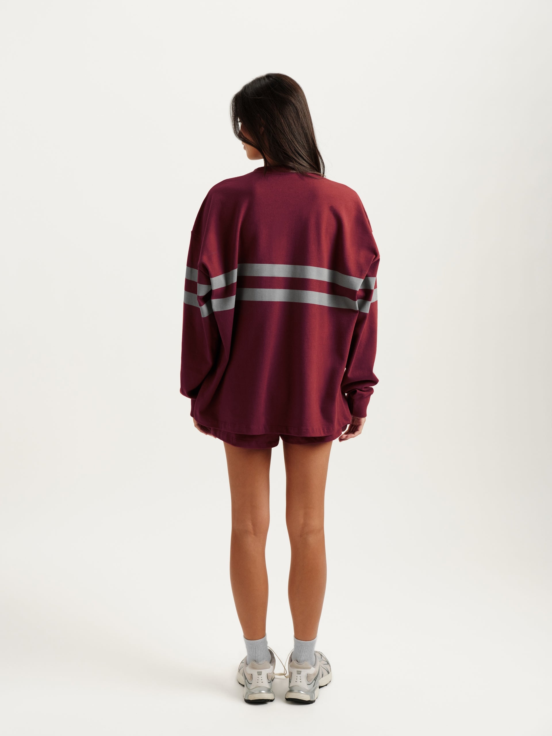 Person wearing a maroon sweater with reflective stripes on a white background