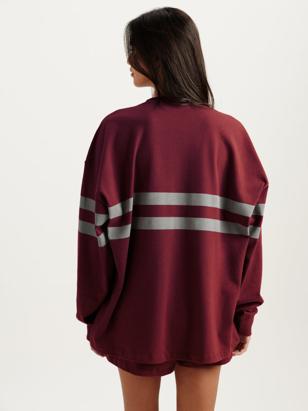 Maroon oversized sweater with white stripes on a plain background