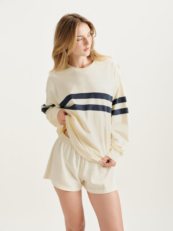 Woman wearing a cream-colored loungewear set with navy stripes on a white background 