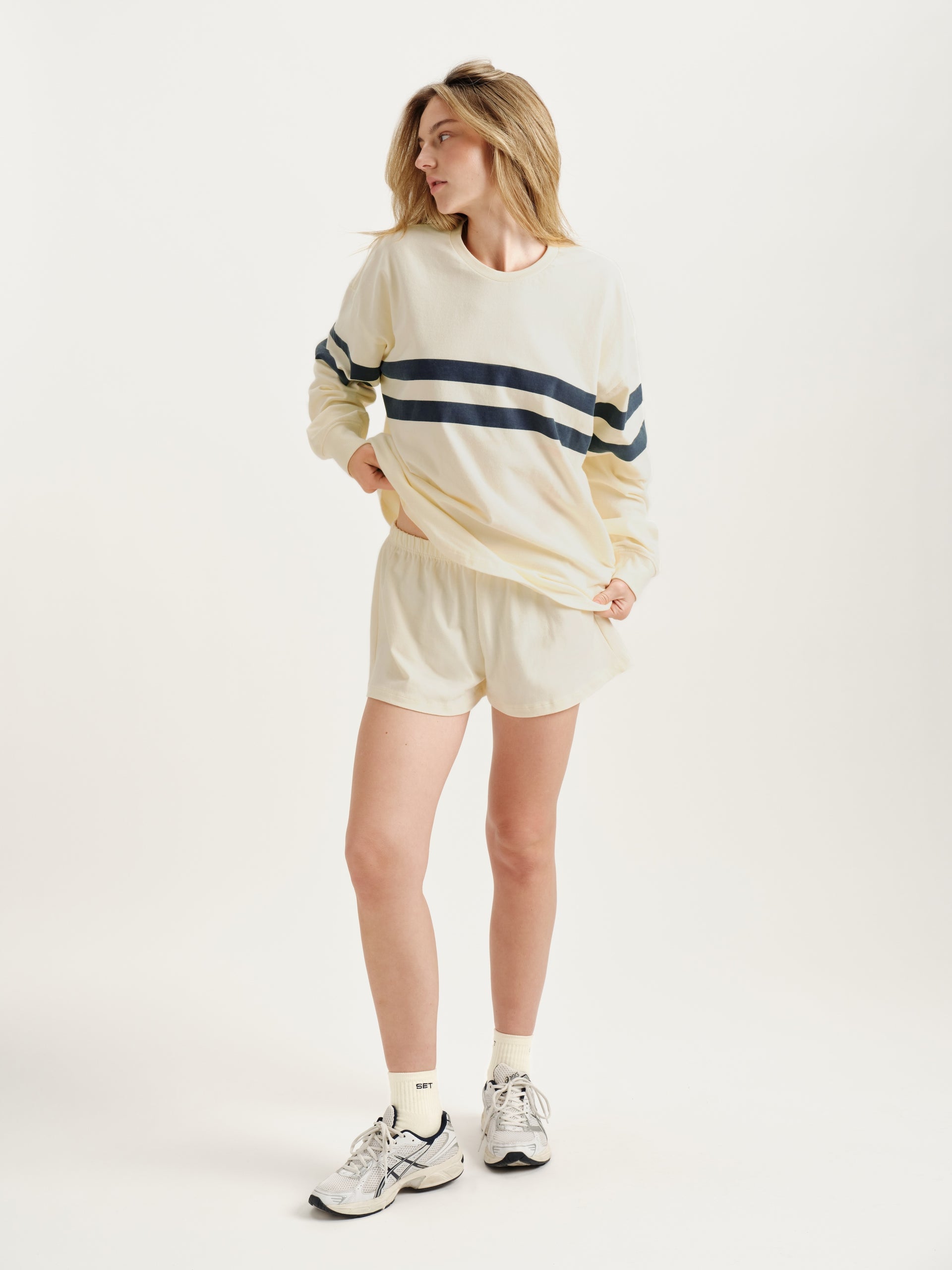 Woman wearing a cream-colored sweatshirt with navy stripes and shorts on a white background <model-info>Alyssa wears a size S and is 5’9, 23” waist, 32B bust.</model-info>
