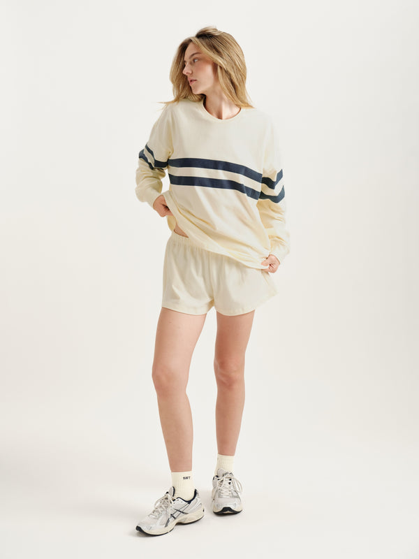 Woman wearing a cream-colored sweatshirt with navy stripes and shorts on a white background 