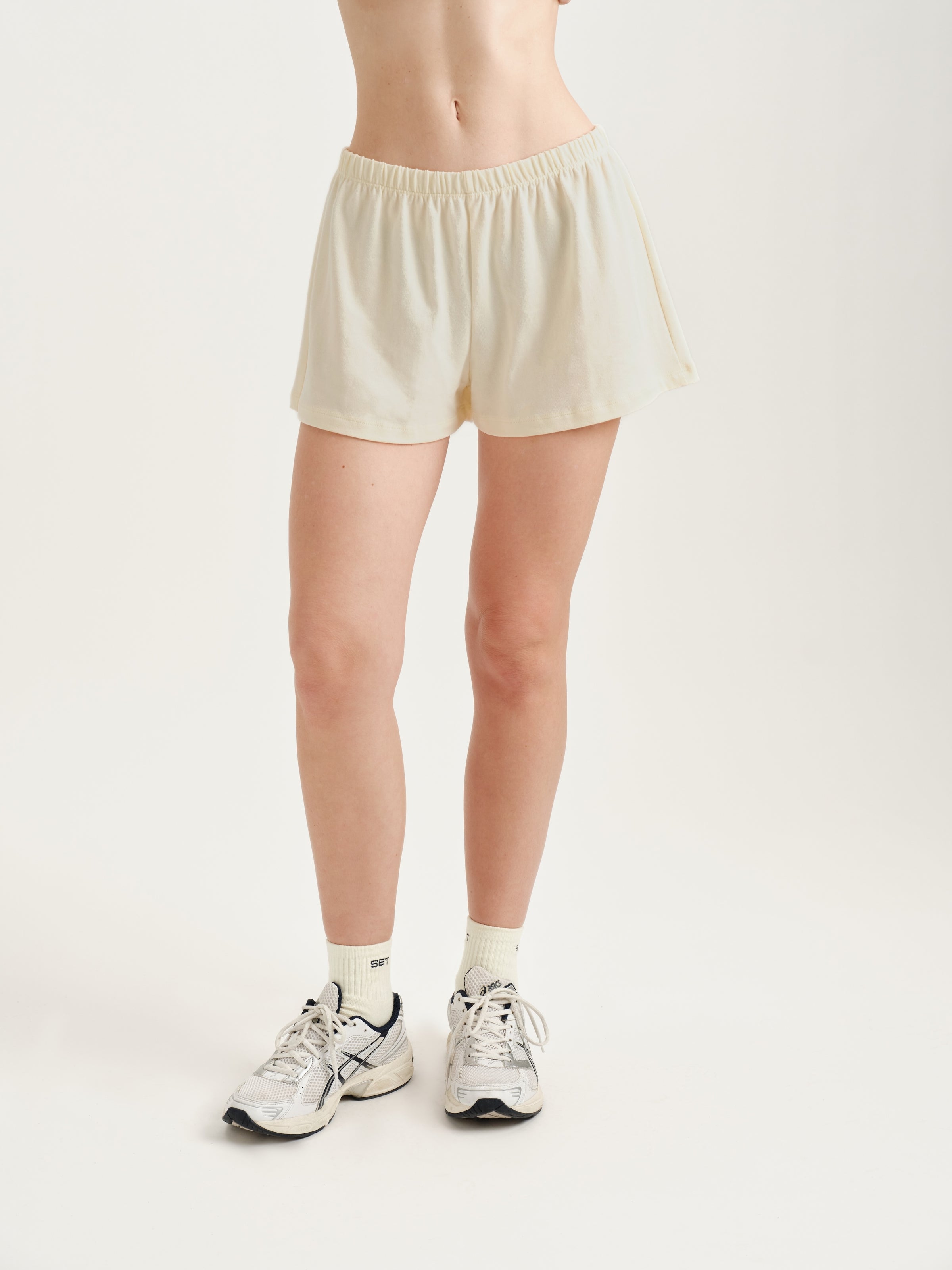 Person wearing cream shorts on a plain background