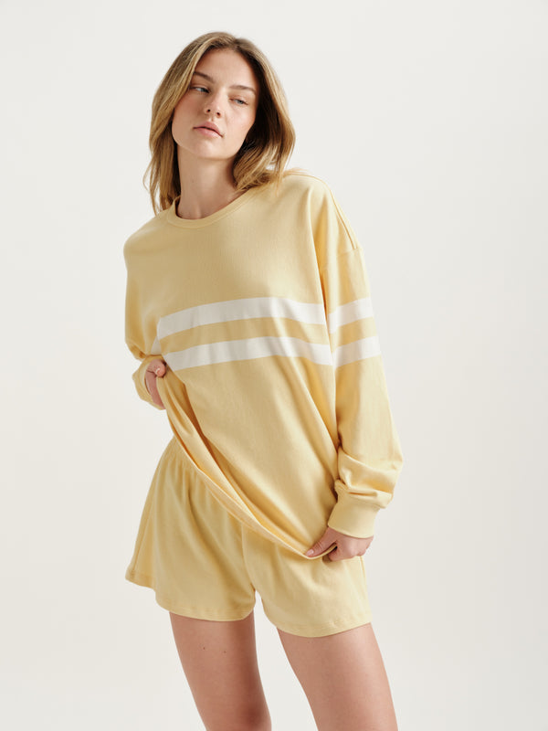 Woman wearing a yellow loungewear set with a white stripe on a light background 