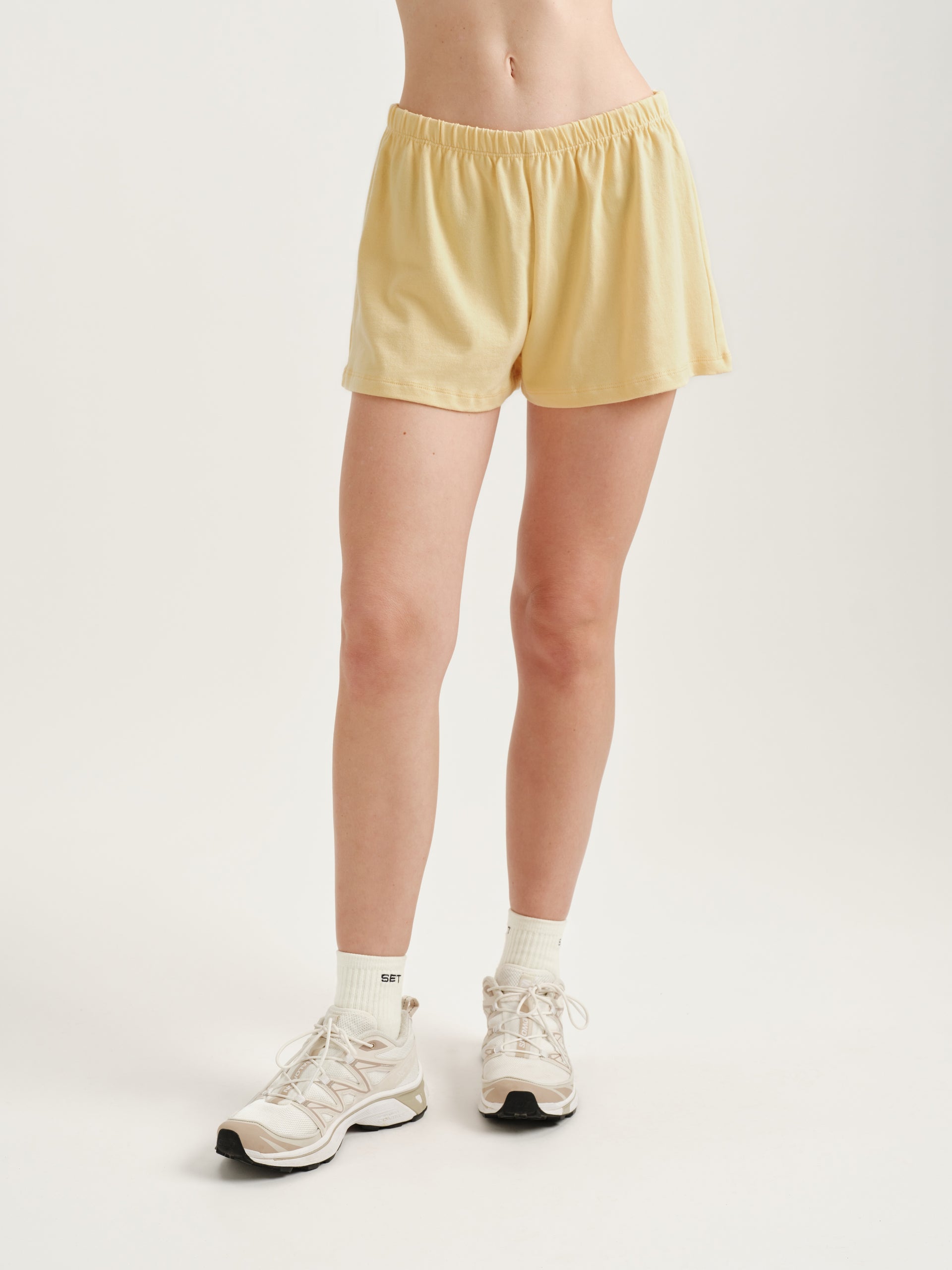 Person wearing yellow shorts and white sneakers on a plain background