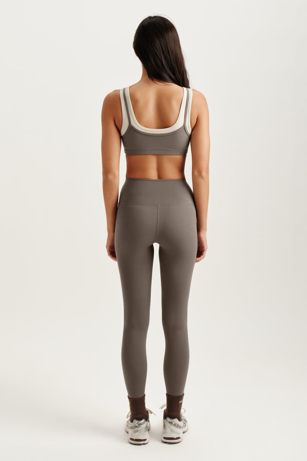 Person wearing a gray sports bra and leggings set on a white background