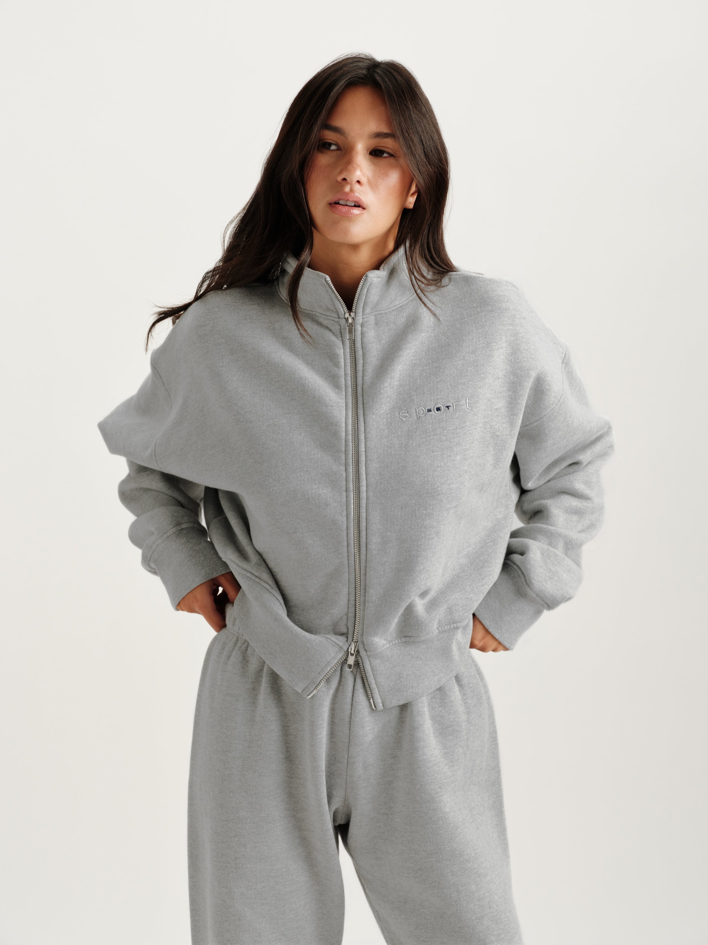 Person wearing a gray zip-up hoodie and pants on a white background 