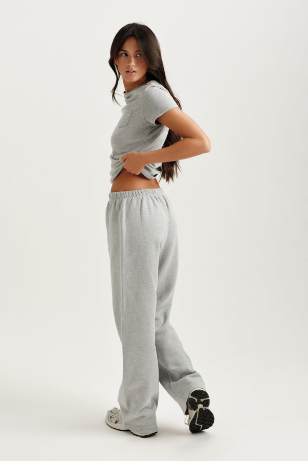 Woman wearing a gray t-shirt and sweatpants on a white background