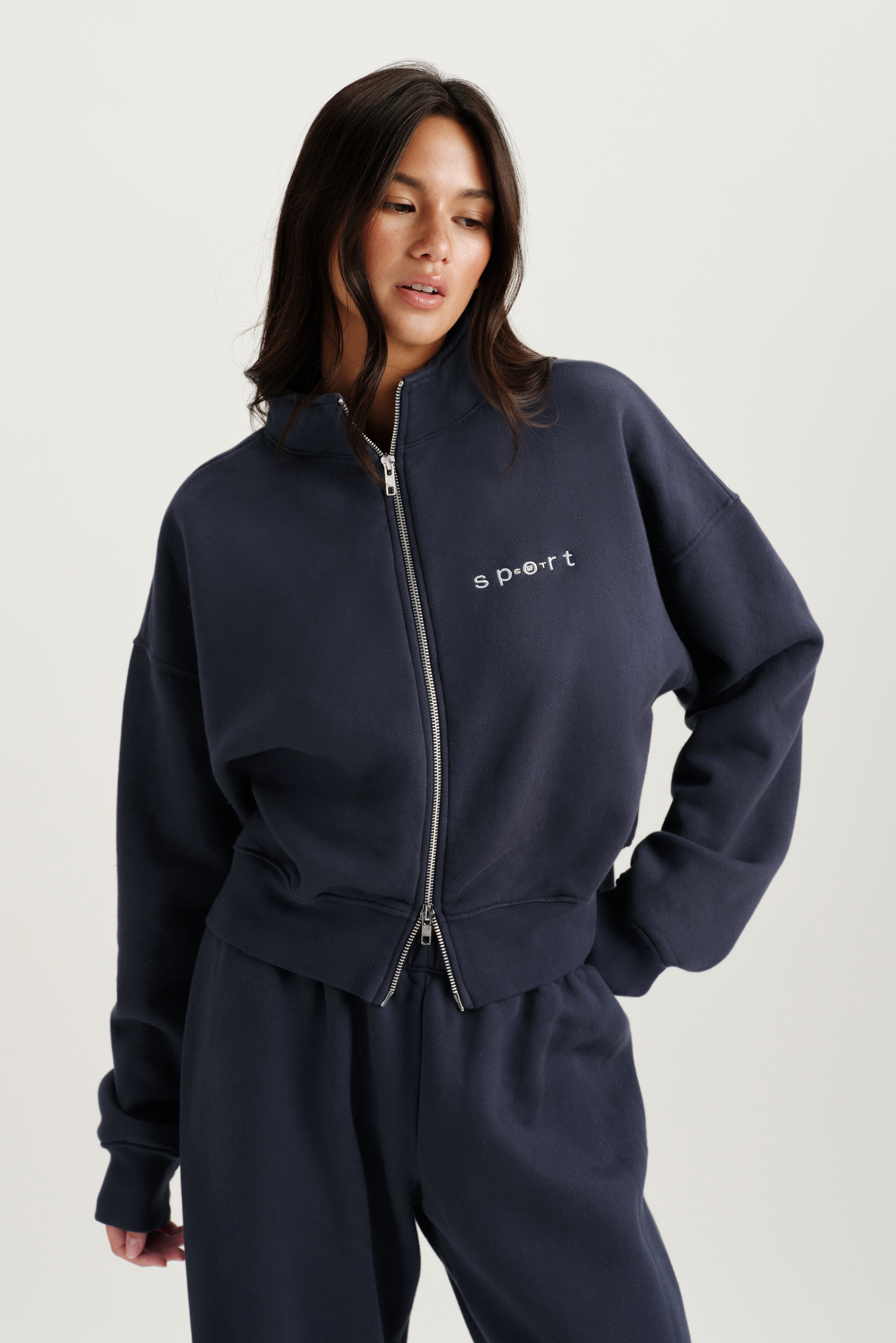 Woman wearing a navy tracksuit with a brand logo on a light gray background 