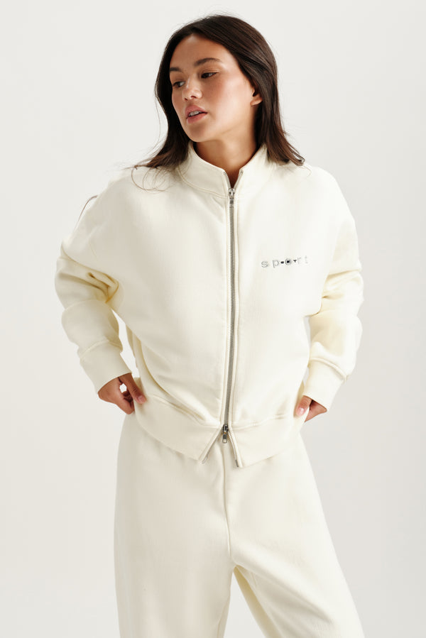 Woman wearing a cream-colored sweat set against a white background 