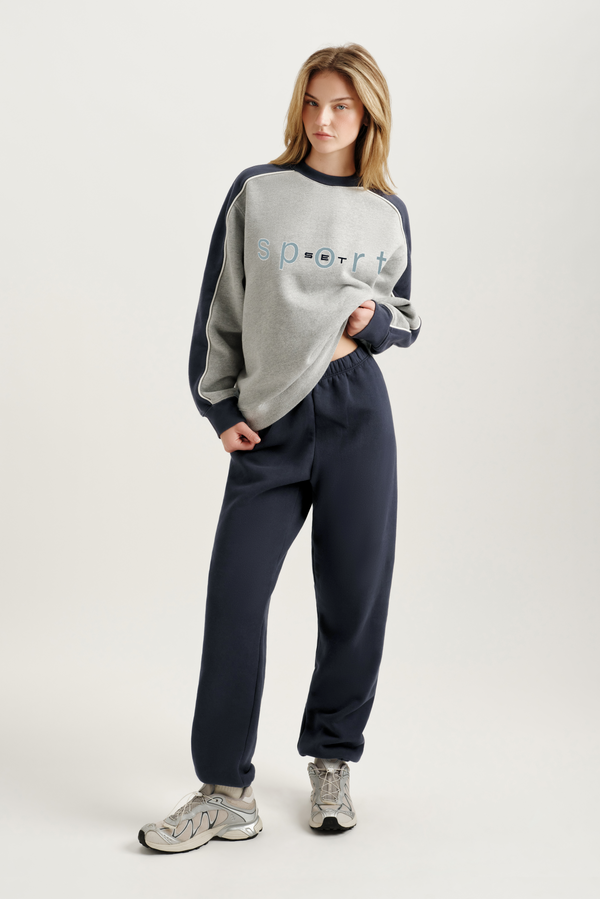 Person wearing a gray and navy tracksuit with 'sport' text on a white background 
