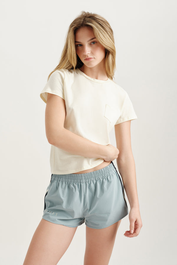 Woman wearing a white t-shirt and light blue shorts on a plain background 