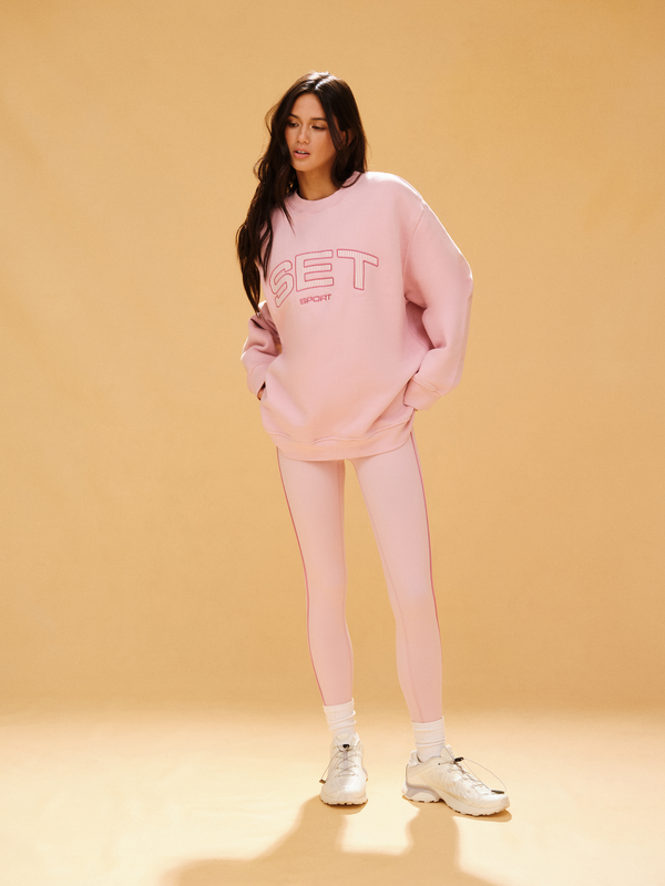 Woman wearing a pink 'SET' sweatshirt and pants on a beige background