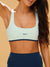 Woman wearing a light blue sports bra with 'SET' branding on a beige background