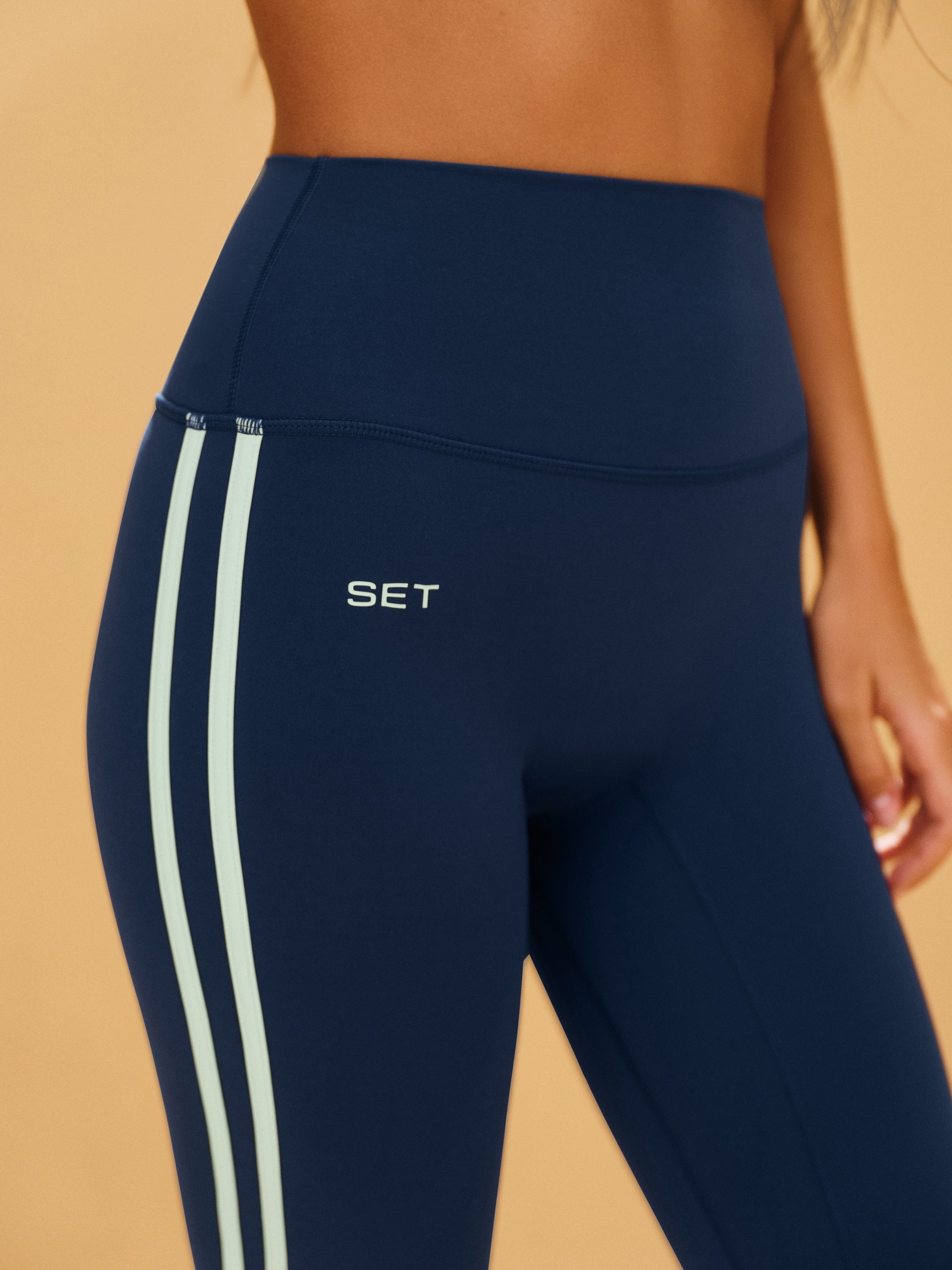 Navy blue leggings with white stripes and 'SET' logo on a beige background