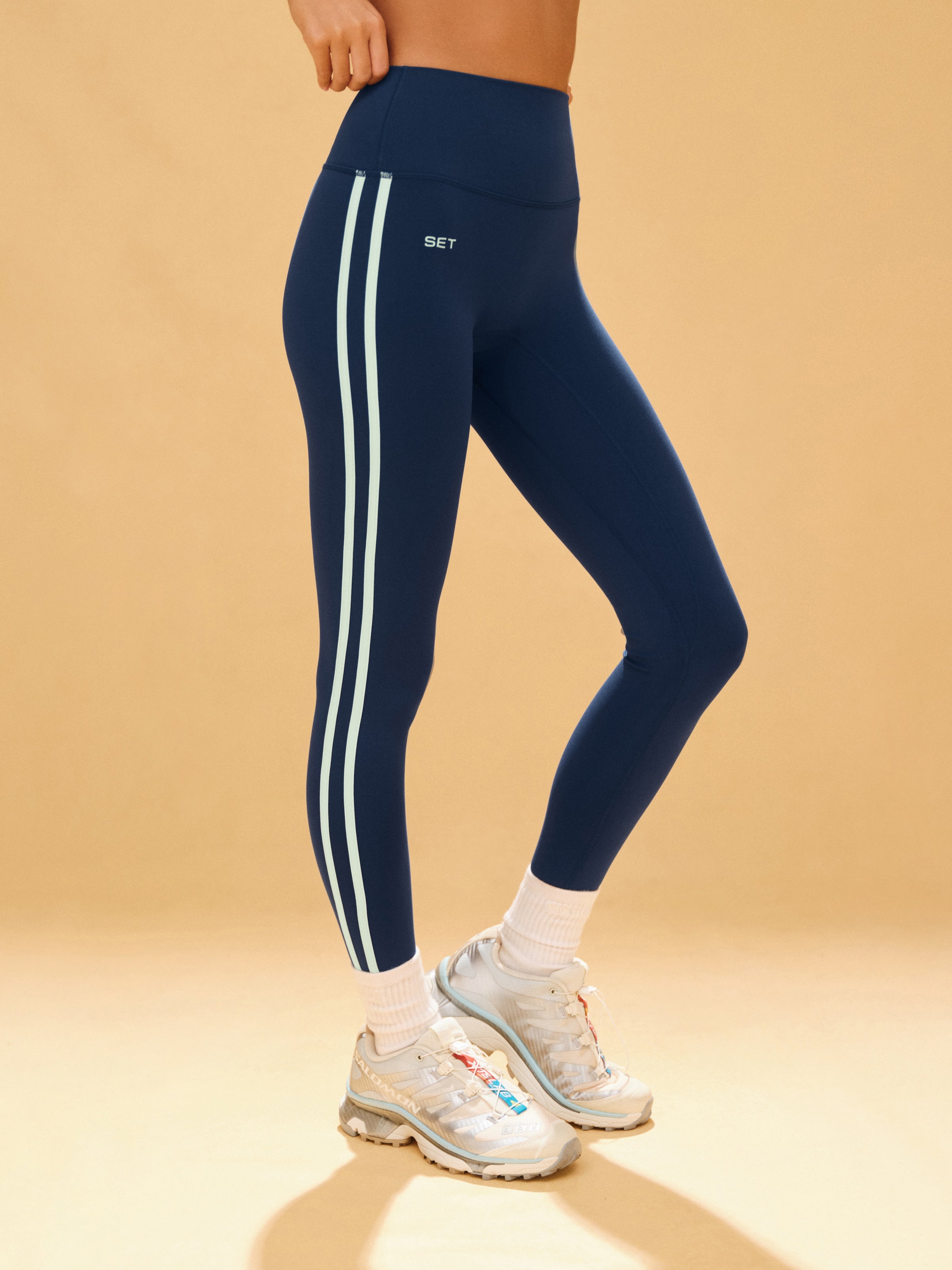 Navy blue leggings with white stripes worn by a person on a beige background