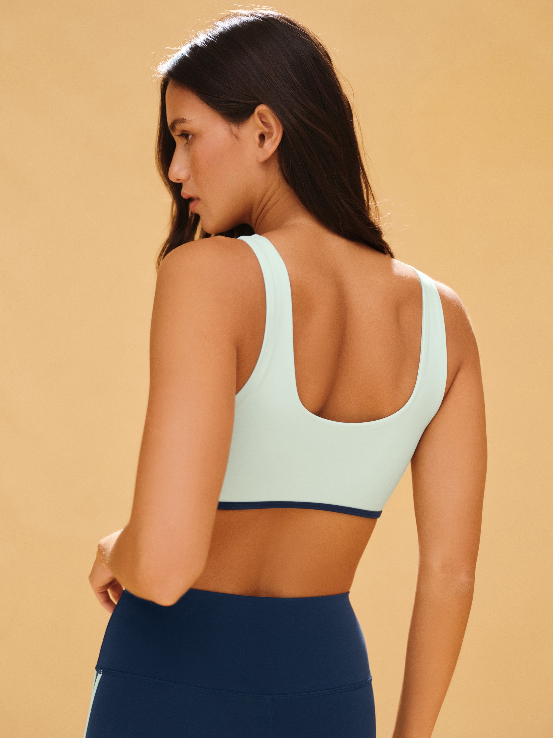 Woman wearing a light blue sports bra and navy leggings on a beige background