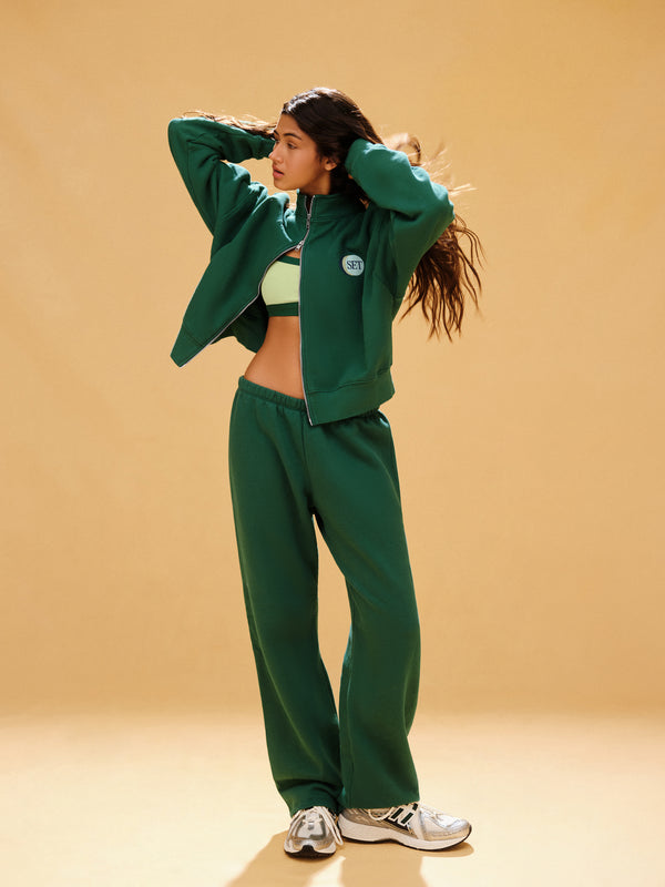 Woman wearing a green tracksuit against a beige background 