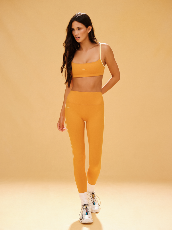 Woman wearing a yellow sports bra and leggings set on a beige background