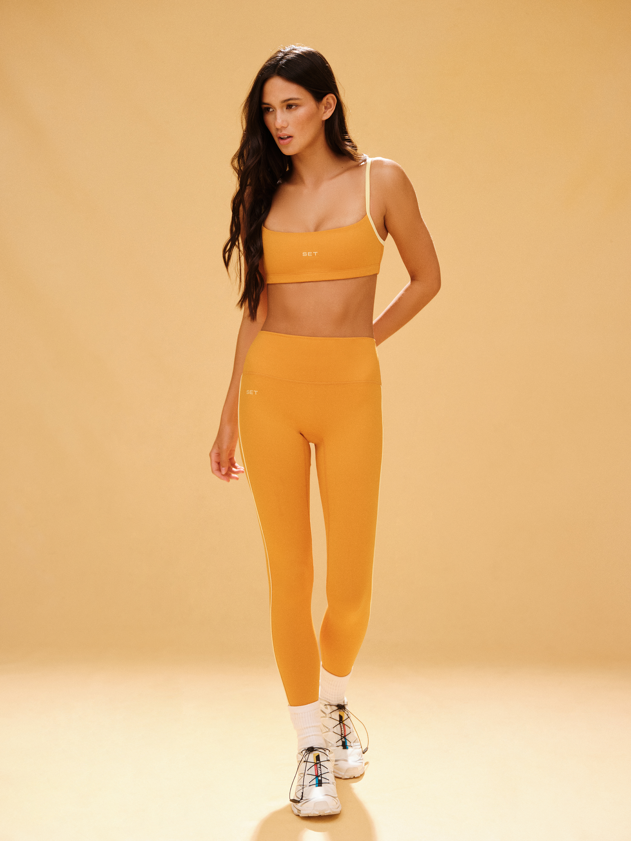 Woman wearing a yellow sports bra and leggings set on a beige background
