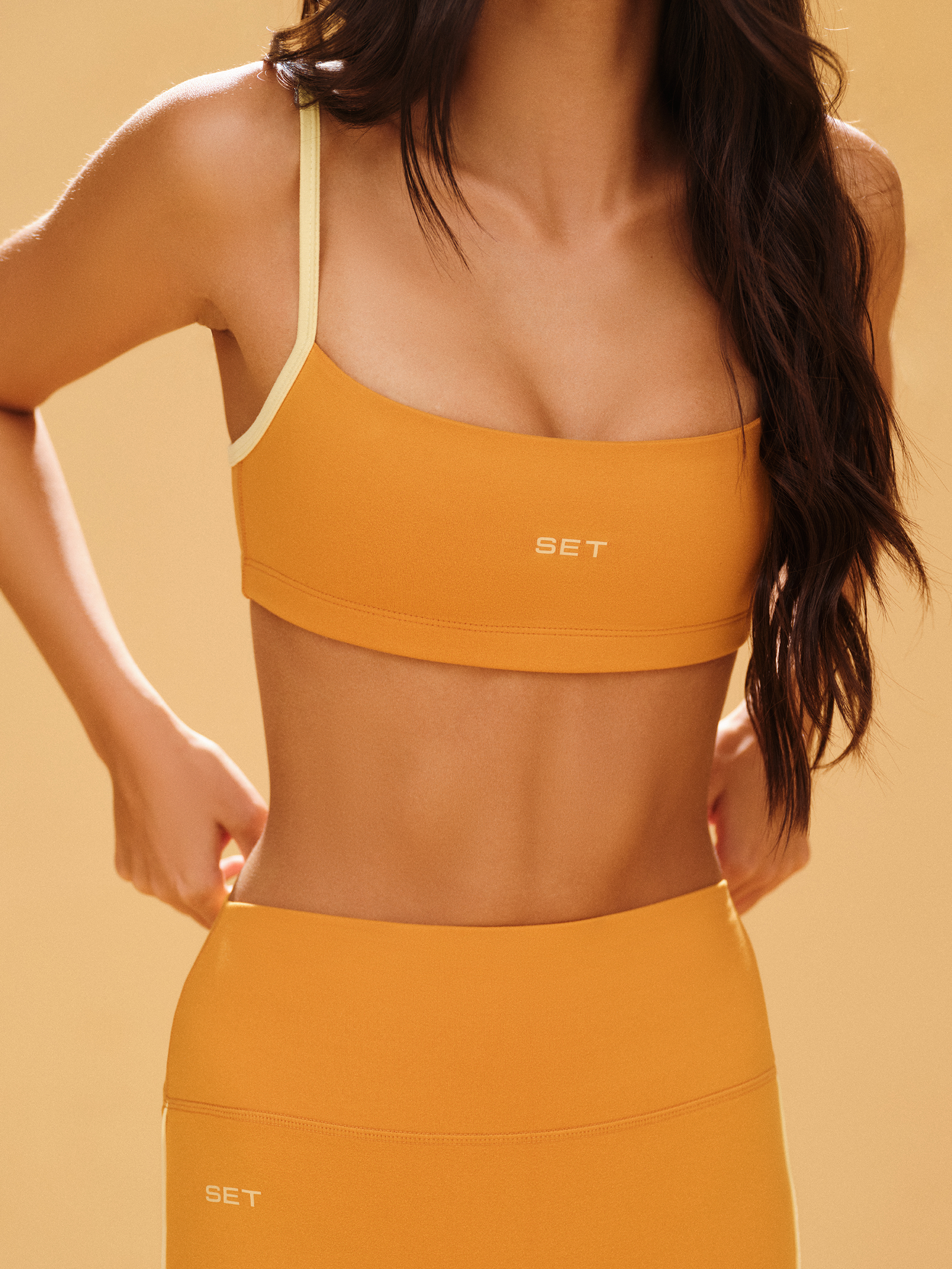 Woman wearing a mustard yellow sports bra and leggings set against a beige background <model-info>Jelene wears a size XS and is 5’7”, 23” waist, 32AB bust.</model-info>