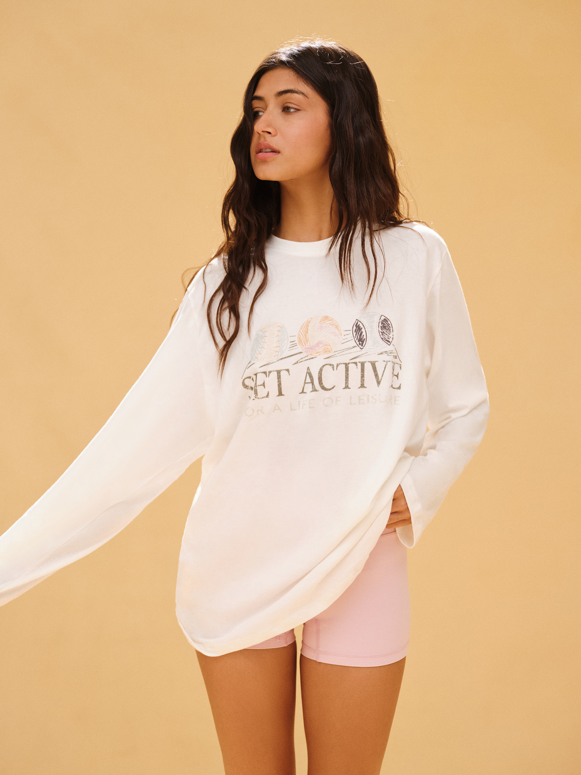 Woman wearing a white oversized sweatshirt with text on a beige background <model-info>Meeya wears a size XS and is 5’7, 23” waist, 32B bust.</model-info> 