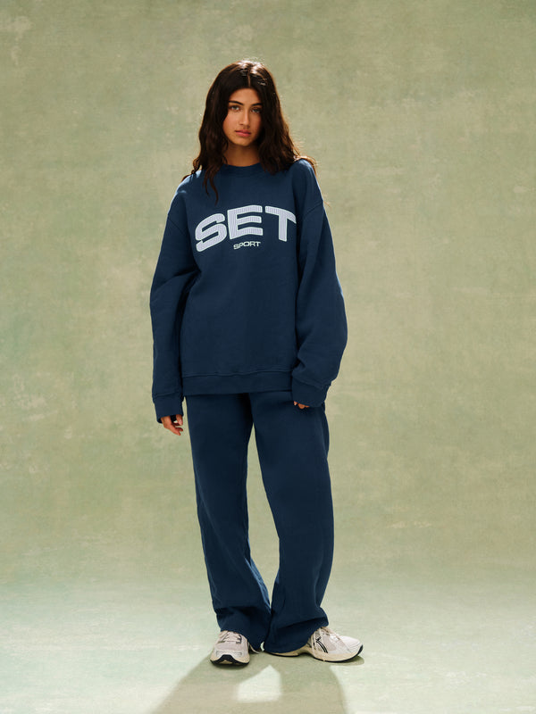 Person wearing a navy blue 'SET' sweatshirt and pants on a plain background