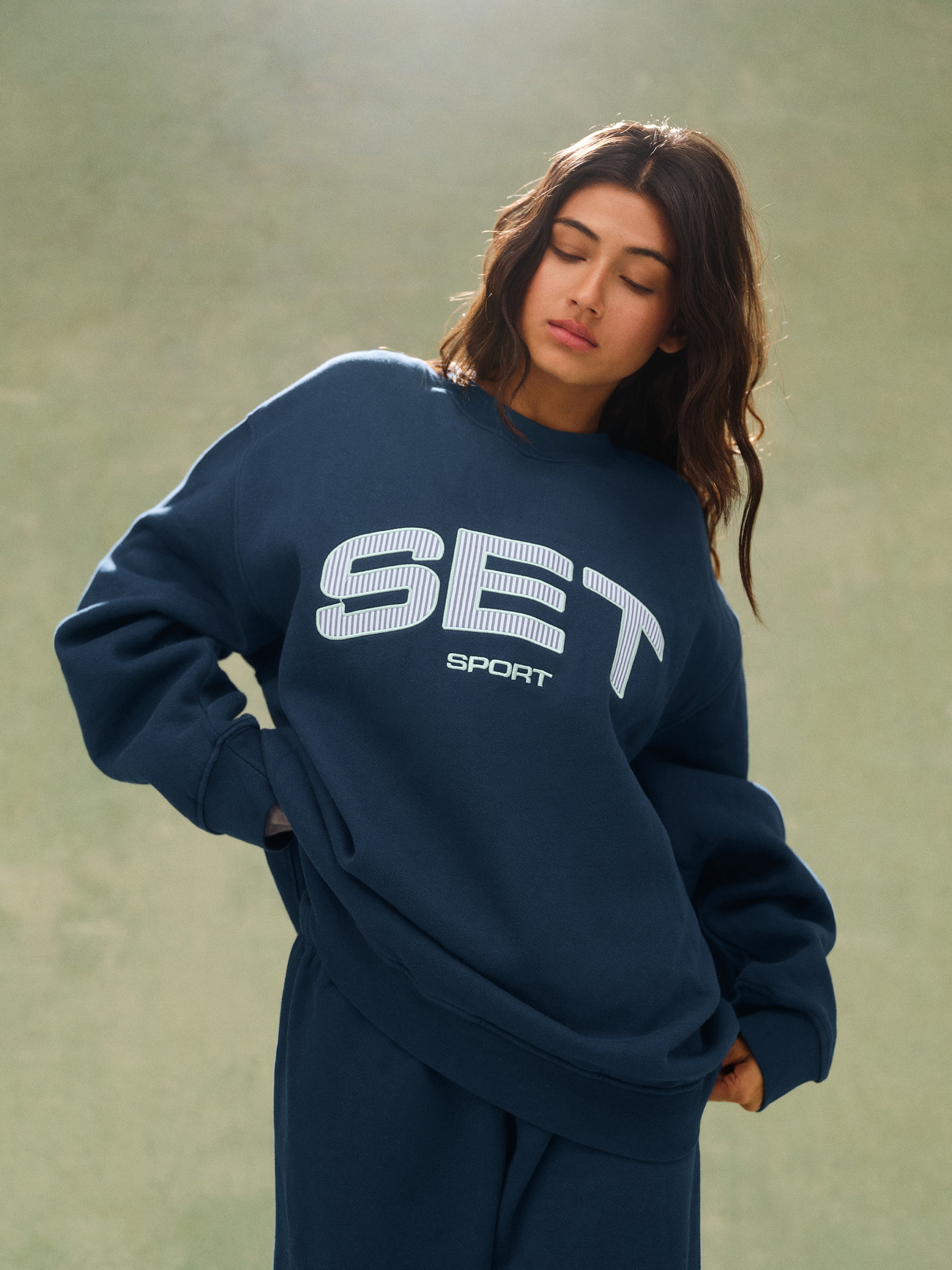 Person wearing a navy blue 'SET Sport' sweatshirt against a green background 